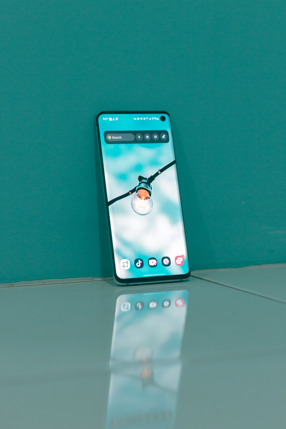 Smartphone with lightbulb wallpaper leaning against a teal wall.